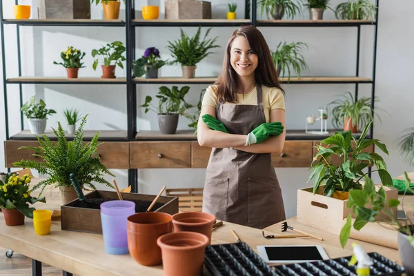 Smiling florist in gloves looking at camera near digital tablet and gardening tools in flower shop — Stock Photo