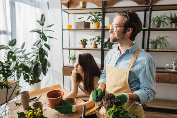 Smiling florists planting flowers and looking away in flower shop — Stock Photo