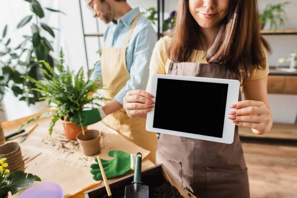 Florista em avental segurando tablet digital com tela em branco perto colega borrado e plantas na loja de flores — Fotografia de Stock