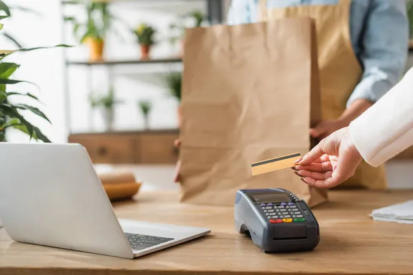 Vista recortada del cliente que paga con tarjeta de crédito cerca del ordenador portátil y floristería borrosa en la tienda de flores - foto de stock