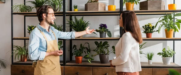 Florist pointing at plants near customer in flower shop, banner — Stock Photo