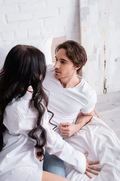 Young man in white t-shirt looking at sensual brunette woman in bedroom — Stock Photo