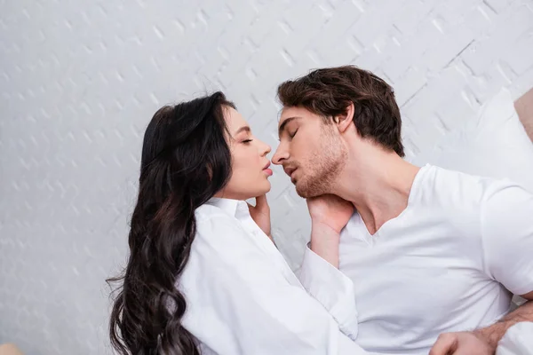 Sexy pareja joven besándose con los ojos cerrados en el dormitorio - foto de stock