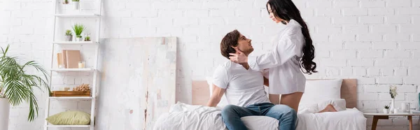 Passionate woman seducing young man sitting on bed in jeans, banner — Stock Photo