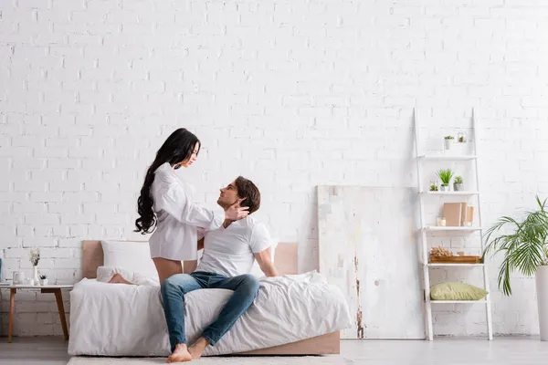 Sinnliche Frau im weißen Hemd verführt jungen Mann im geräumigen Schlafzimmer — Stockfoto
