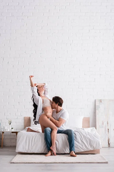 Young man kissing body of sexy woman in white shirt and underwear in bedroom — Stock Photo