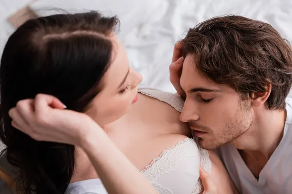 Man with closed eyes near breast of seductive woman in bra on blurred foreground — Stock Photo