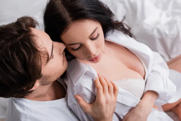 Vista aérea de hombre joven abrazando a mujer morena en camisa blanca y sujetador - foto de stock