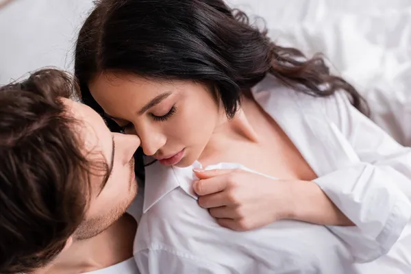 Seductora morena mujer con los ojos cerrados cerca de hombre joven en el dormitorio — Stock Photo