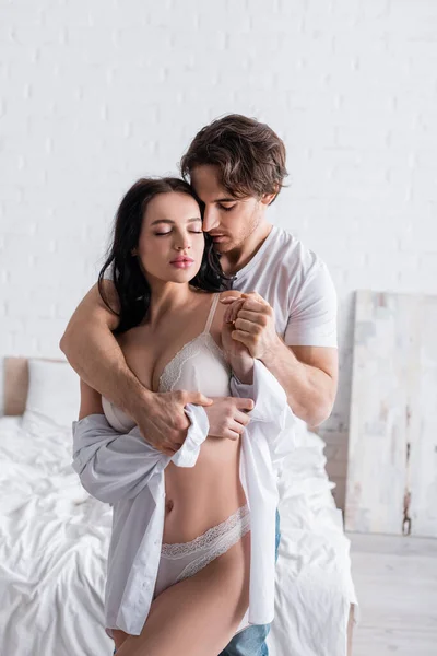 Young man holding hand and embracing sexy woman in underwear in bedroom — Stock Photo