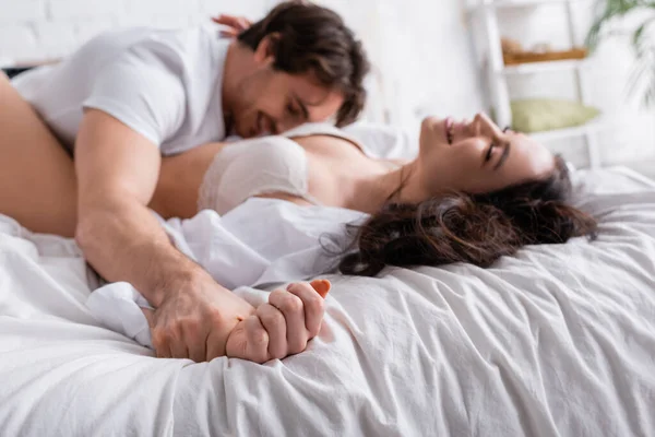 Borrosa pareja sonriendo mientras yacen juntos en ropa de cama blanca - foto de stock