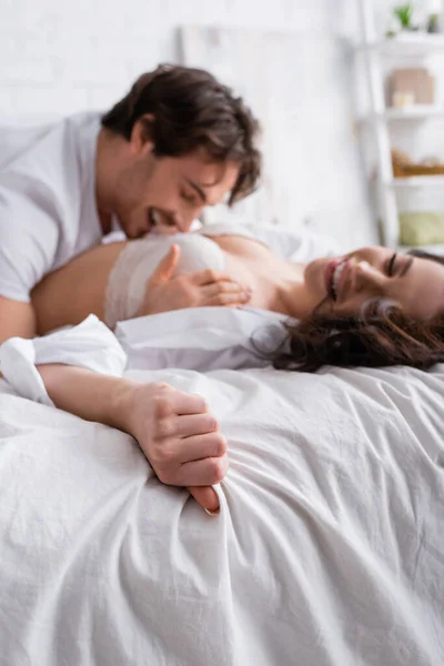 Felice uomo abbracciando sorridente fidanzata su biancheria da letto bianca, sfondo sfocato — Foto stock
