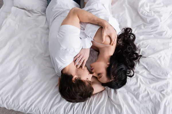 Vista superior de casal jovem apaixonado com olhos fechados abraçando em roupa de cama branca — Fotografia de Stock