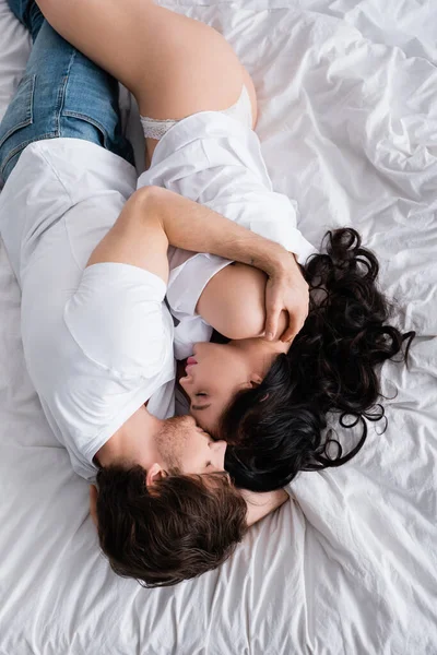 Overhead view of man in jeans hugging sexy woman in shirt and panties on bed — Stock Photo