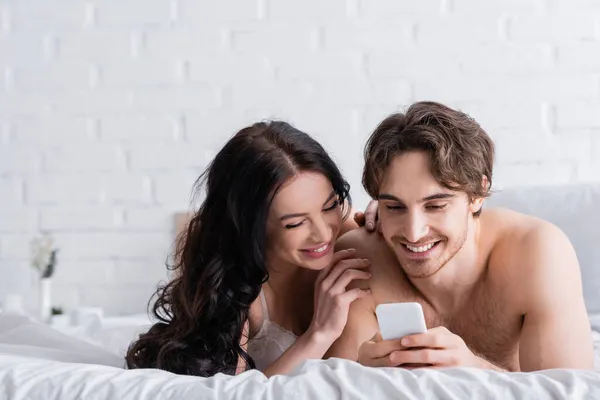 Alegre jovem casal usando smartphone na cama de manhã — Fotografia de Stock