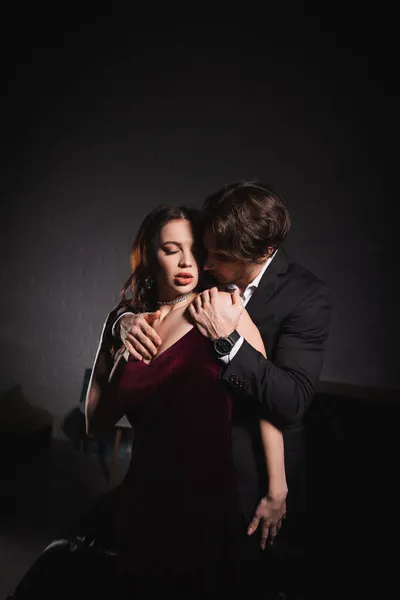 Mujer apasionada en vestido elegante cerca del hombre en traje seduciéndola en la oscuridad - foto de stock