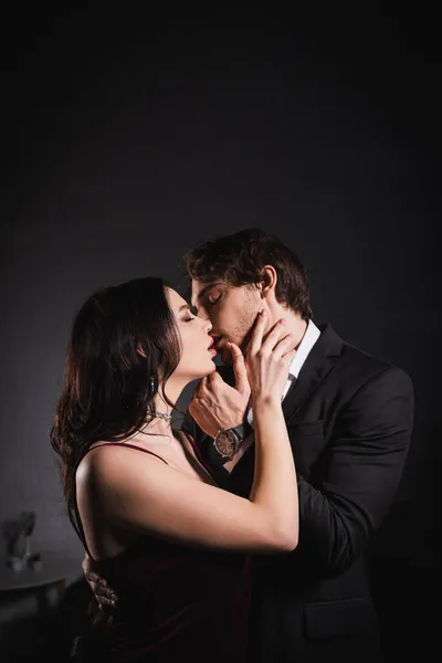 Uomo in giacca e cravatta e donna sensuale in abito elegante baciarsi con gli occhi chiusi di notte — Foto stock