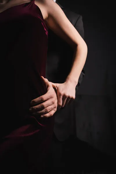 Обрізаний вид чоловіка торкається стегна елегантної жінки в темряві — стокове фото