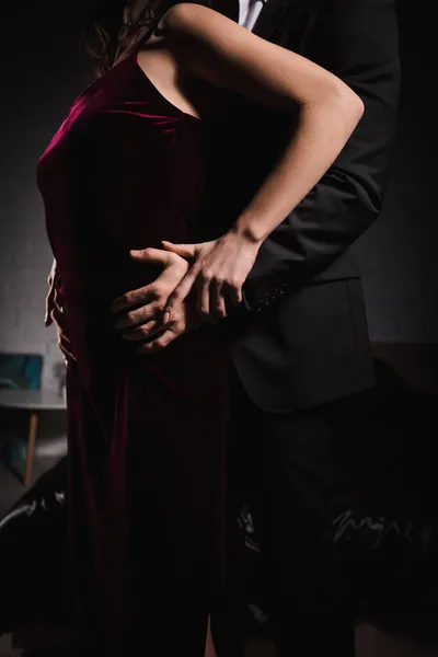 Partial view of man seducing woman in elegant dress while hugging her hips at night in bedroom — Stock Photo