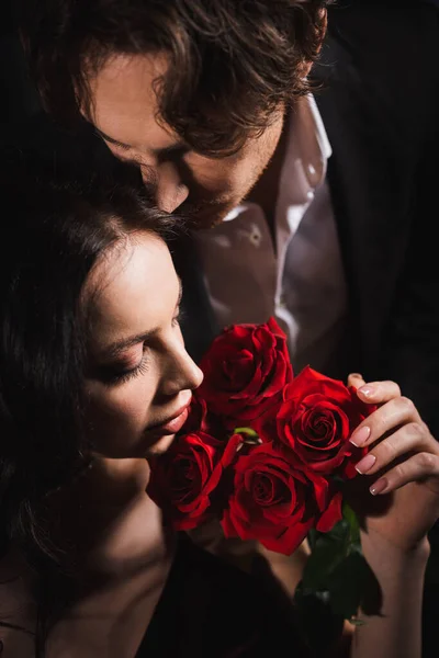 Close up view of sensual woman holding red rosed near young man in black suit — Stock Photo