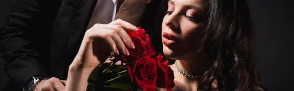 Jovem e sedutora mulher com rosas vermelhas perto do homem em preto, bandeira — Fotografia de Stock