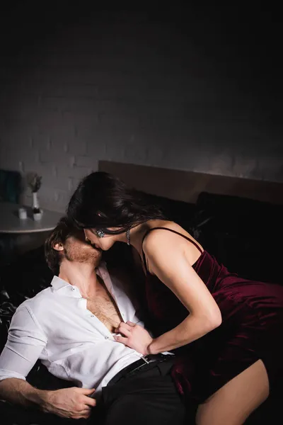 Brunetta donna in abito elegante baciare l'uomo in camicia bianca su biancheria da letto nera — Foto stock