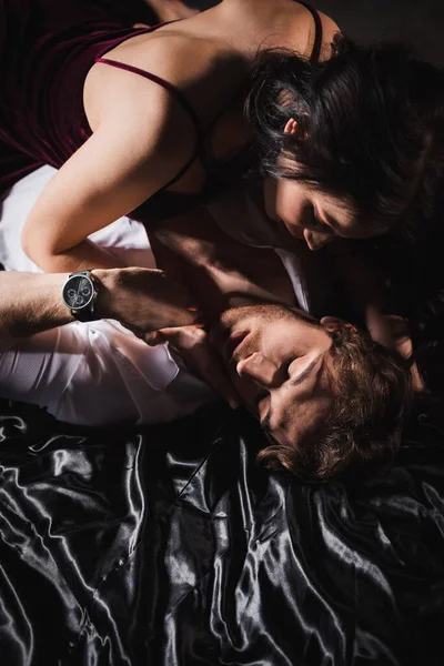 Vue grand angle d'un couple élégant et passionné embrassant sur une literie en soie noire — Photo de stock