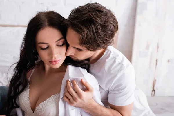 Young man seducing sensual woman in white shirt and bra in bedroom — Stock Photo