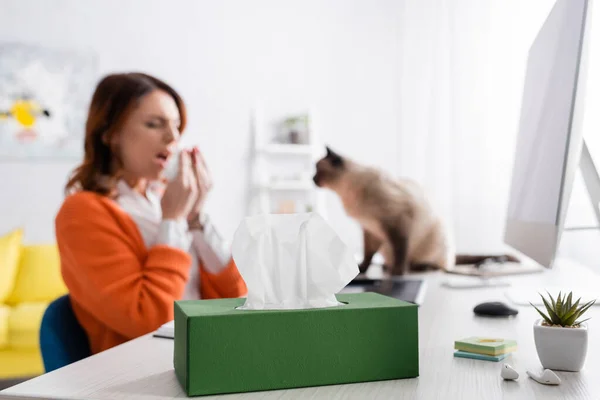 Donna allergica offuscata starnutisce vicino al gatto e confezione di tovaglioli di carta sulla scrivania — Foto stock