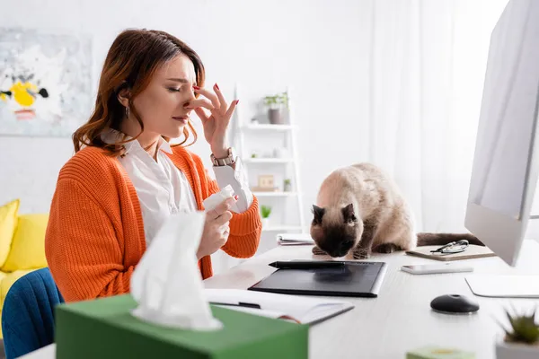 Allergic woman sneezing near cat sitting on work desk near graphic tablet — Stock Photo