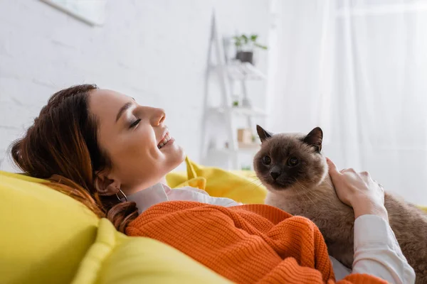 Side view of happy woman with closed eyes relaxing with cat on couch — Stock Photo