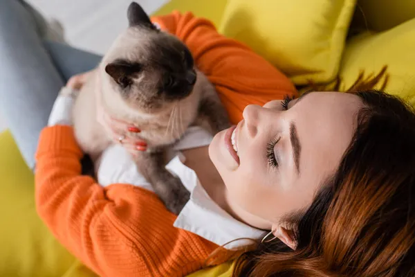 Vista aérea de la mujer sonriente con los ojos cerrados sentado con gato en el sofá - foto de stock