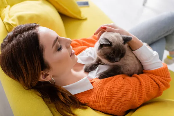 Vista de ángulo alto de la joven sentada con gato en sofá amarillo - foto de stock