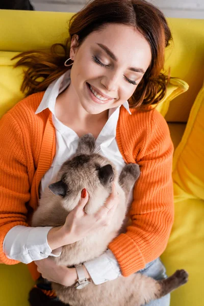 Vue grand angle de femme joyeuse avec les yeux fermés relaxant avec chat sur le canapé — Photo de stock