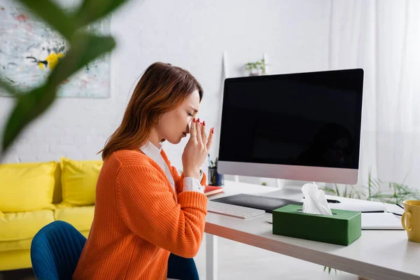 Freelancer doente espirra em guardanapo de papel enquanto trabalha perto do monitor com tela em branco — Fotografia de Stock