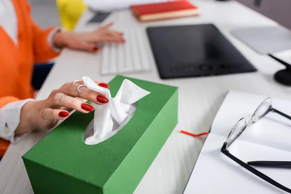 Vue recadrée du pigiste prenant une serviette en papier du paquet près des appareils sur le bureau — Photo de stock