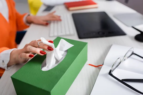 Visão recortada do freelancer levando guardanapo de papel do pacote perto de dispositivos na mesa — Fotografia de Stock