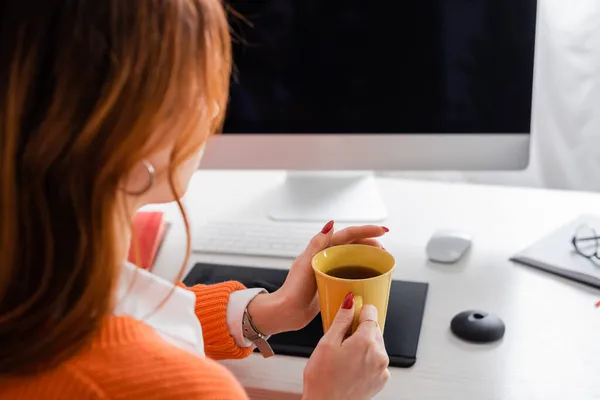 Retuscher hält Tasse Tee in der Nähe verschwommenes Grafik-Tablet und Monitor mit leerem Bildschirm — Stockfoto