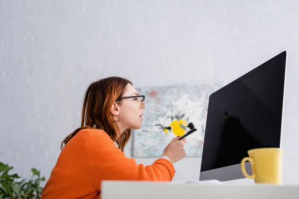Freelancer concentrado em óculos apontando para monitor com tela em branco enquanto trabalhava em casa — Fotografia de Stock