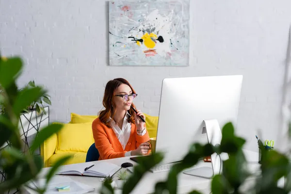 Durchdachte Retusche, die Stift hält, während sie in der Nähe von Grafik-Tablet und Monitor auf unscharfem Vordergrund arbeitet — Stockfoto