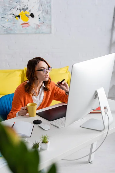 Retusche mit Tasse Tee zeigt bei der Arbeit zu Hause auf Monitor mit Stift — Stockfoto