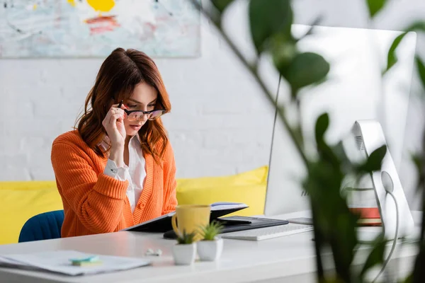 Junge Designerin justiert Brille, während sie zu Hause auf verschwommenem Vordergrund arbeitet — Stock Photo