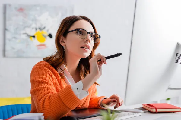 Retoque en gafas graduadas apuntando con lápiz óptico al monitor mientras se trabaja con tableta gráfica - foto de stock