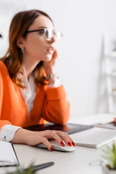 Designer desfocado em óculos usando o mouse do computador enquanto trabalhava perto de tablet gráfico em casa — Fotografia de Stock