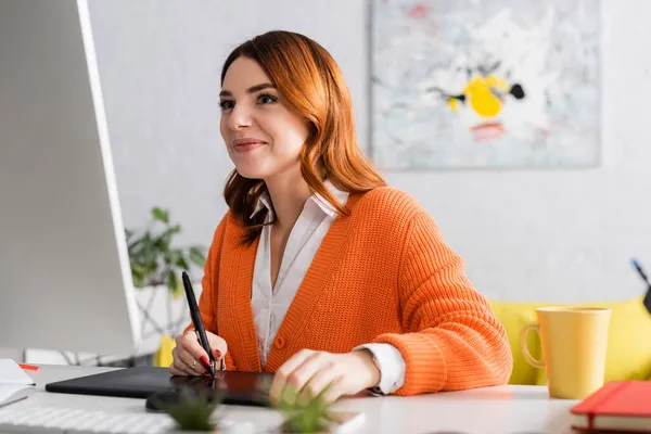 Retoque sonriente mirando el monitor de la computadora mientras se trabaja en la tableta gráfica - foto de stock