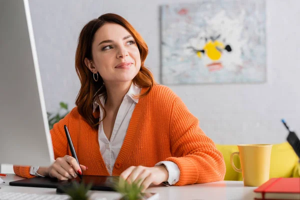 Happy designer looking away while working on graphic tablet at home — Stock Photo