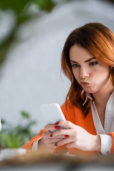 Unzufriedene Frau benutzt Smartphone zu Hause im verschwommenen Vordergrund — Stock Photo