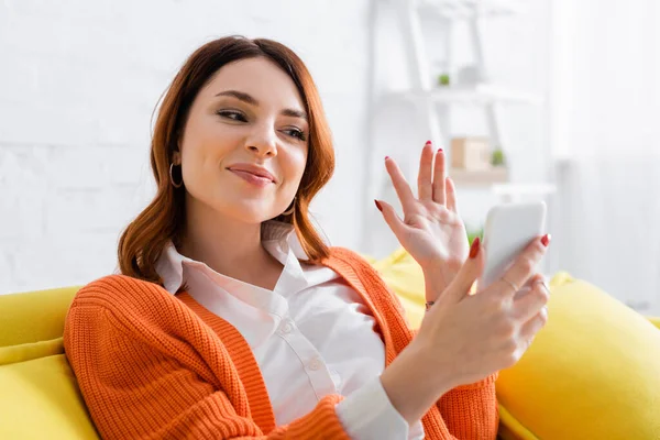 Mulher sorrindo acenando a mão durante a chamada de vídeo no celular em casa — Fotografia de Stock