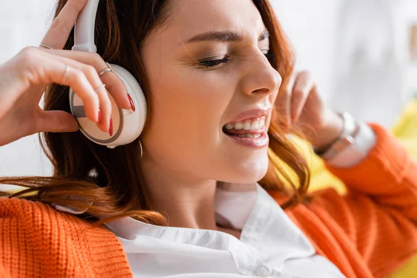 Vista de cerca de la mujer emocionada sobresaliendo de la lengua mientras escucha música en los auriculares - foto de stock