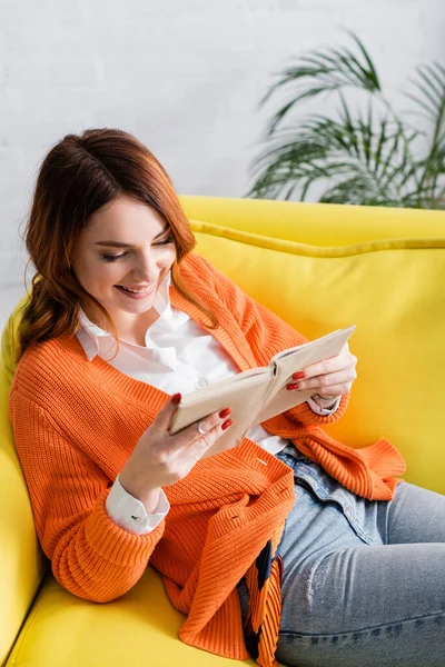 High angle view of joyful woman reading book on yellow couch — Stock Photo